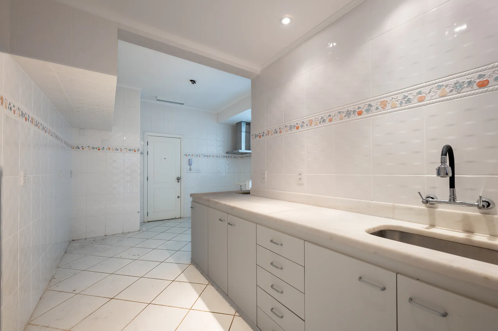 A kitchen in white tiling with a long counter and sink