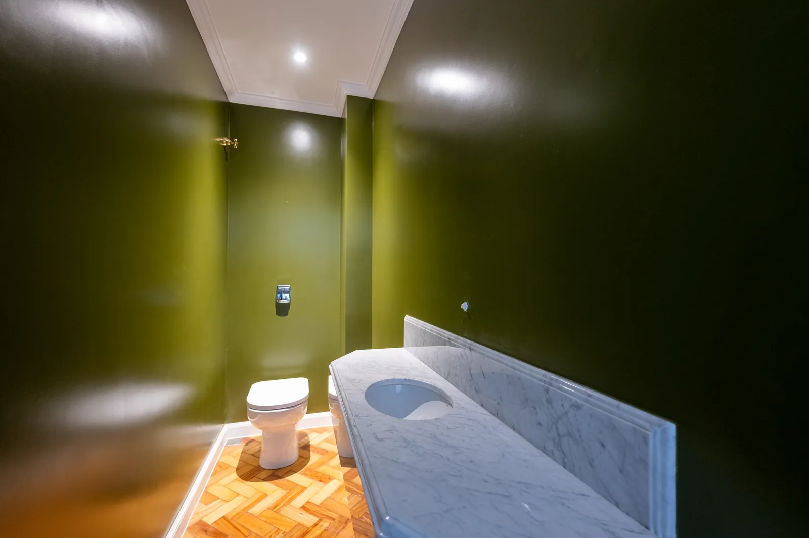 A guest cloakroom with deep green walls and a marble top