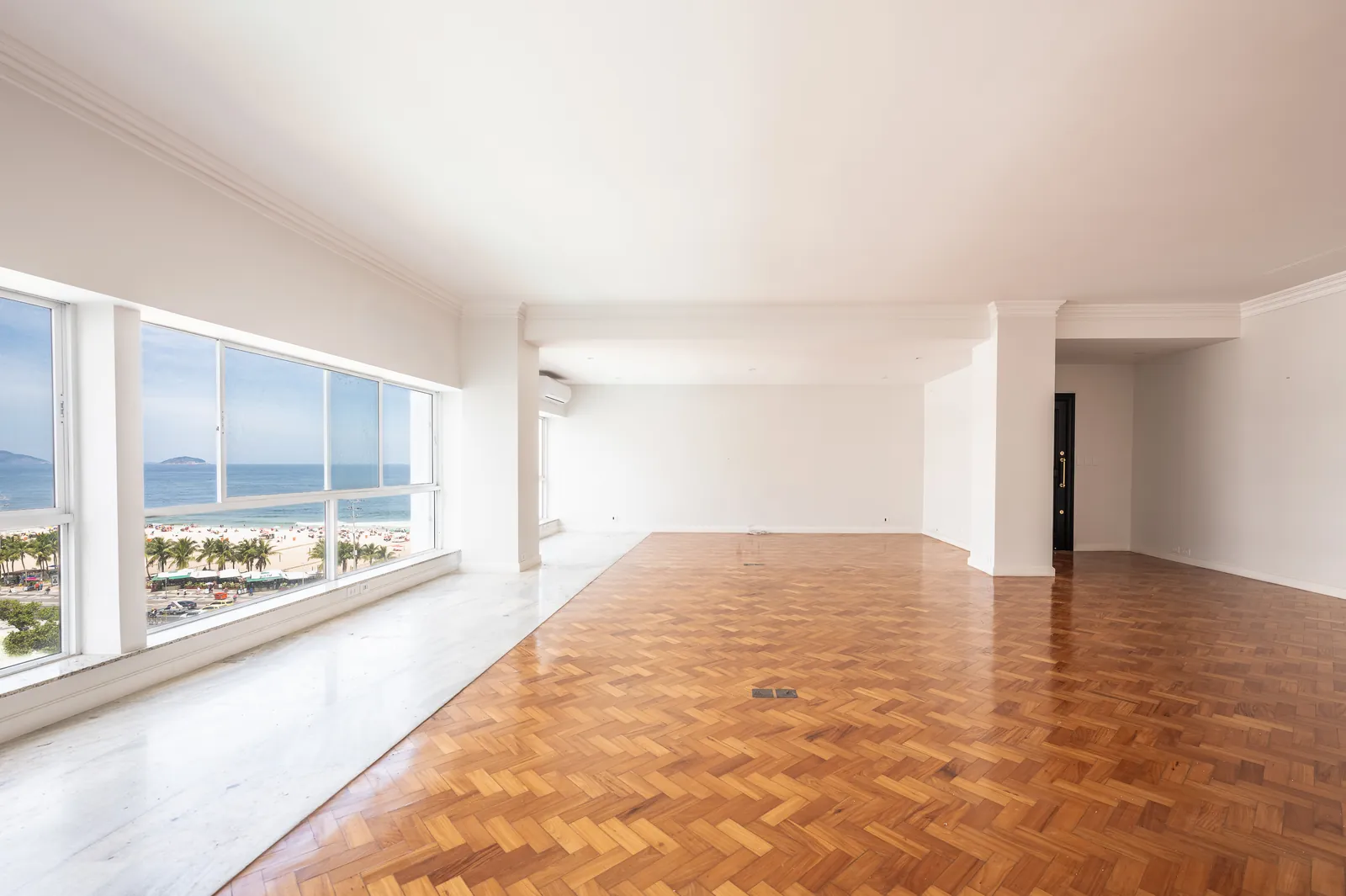 An empty reception room with floor-to-ceiling windows and herringbone parquet